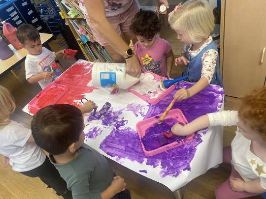 A group of children sitting around a table with purple paint.