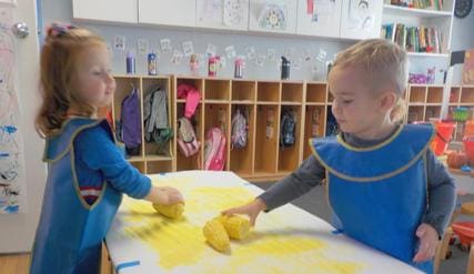 Two children are playing with yellow play dough.